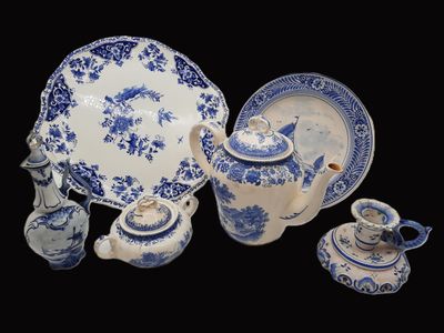 Plusieurs pièces de poterie bleue et blanche sont exposées sur un fond noir
