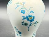 a white vase with blue flowers on it sitting on a table