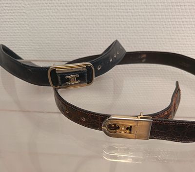 une paire de ceintures en cuir marron et noir, ornées de boucles dorées, exposées