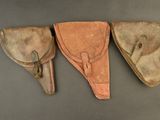 three leather holsters are lined up on a gray surface