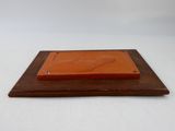 une plaque orange posée sur un socle en bois, avec un fond blanc
