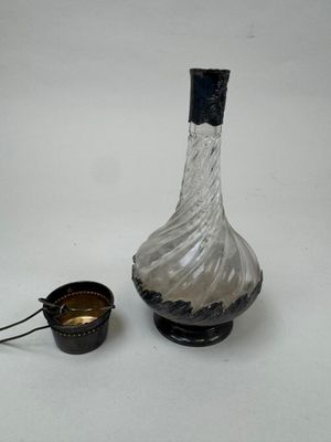 une bouteille en verre avec une poignée noire, à côté d'un petit récipient en métal