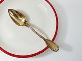 a red and white plate with a gold spoon on it