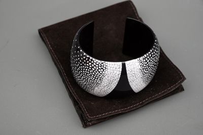 bracelet manchette argenté et noir posé sur un tissu marron, sur une surface grise