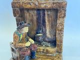 une figurine représentant un homme assis sur un banc devant une cabane