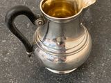 a silver pitcher with a black handle on the ground