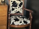 a cow print chair next to a dresser with a lamp on it