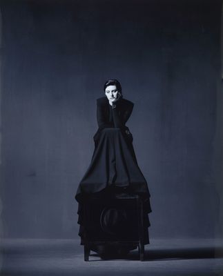 a black and white photo of a woman in a black dress sitting on a chair