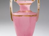 un vase rose avec une anse dorée sur un fond blanc