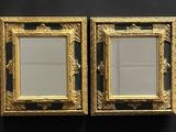 two gold framed mirrors on a black wall next to each other