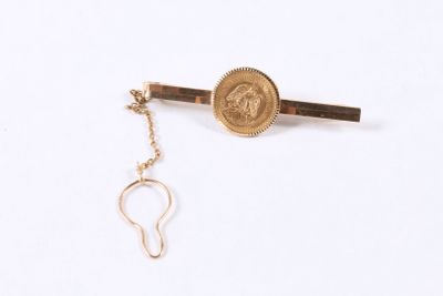 a gold tie bar with a coin attached to it