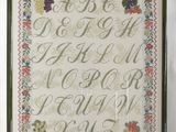 un échantillon de point de croix encadré représentant un alphabet composé de fruits et de légumes