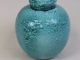 un petit vase bleu muni d'un couvercle, posé sur une surface blanche