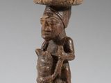 une statue en bois représentant une femme portant un panier sur la tête