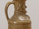 a brown pitcher with a hat on it on a table