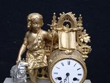 a gold clock sitting on a marble base with a statue of a boy holding a bag