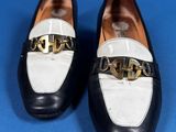 black and white loafers with gold buckles on a blue surface