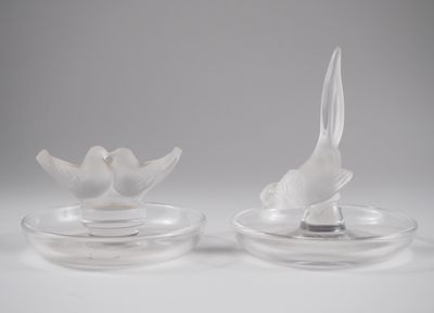 une paire d'oiseaux en verre transparent posés sur une assiette transparente, sur fond blanc