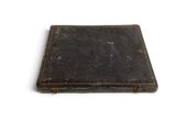 an old black book sitting on top of a table next to a white wall