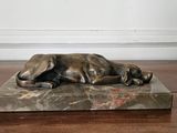 une statue en bronze représentant un chien couché sur un socle en marbre