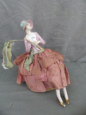 une figurine représentant une femme en robe rose et chapeau, assise sur une chaise