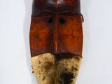 un vieux masque en bois posé sur une surface blanche, avec une longue barbe