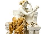 une statue représentant une femme assise sur un banc en train de lire un livre