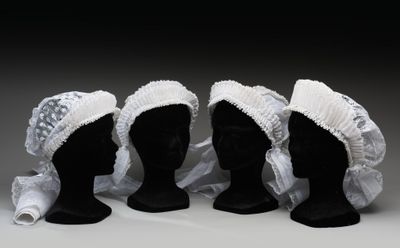 trois têtes de mannequins noires coiffées de bonnets blancs sur fond blanc