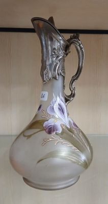un vase en verre muni d'une poignée en argent, posé sur une étagère