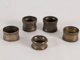 six antique brass napkin holders on a white surface