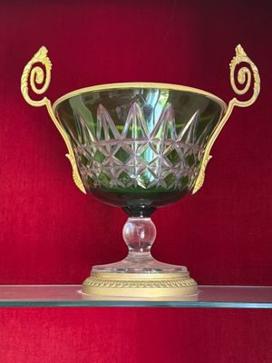un saladier en verre vert posé sur une étagère en verre contre un mur rouge