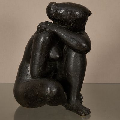 statue d'une femme assise sur une table en verre, les mains posées sur les genoux