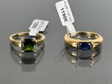 two gold rings with green and blue stones on a black surface