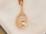 a gold tennis racket and ball on a marble surface