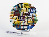 a multicolored plate sitting on a stand with a flower