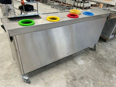 une table en acier inoxydable sur laquelle sont posées trois tasses colorées, dans un entrepôt