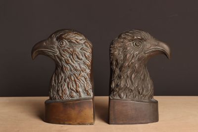 une paire de serre-livres en bronze représentant des têtes d'aigle, posés sur une table en bois