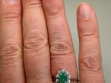 a woman ' s hand holding a green and white diamond ring