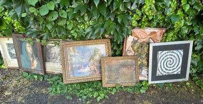 a lot of framed pictures on the ground next to a bush