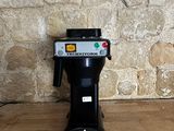 une cafetière posée sur un parquet, près d'un mur en pierre