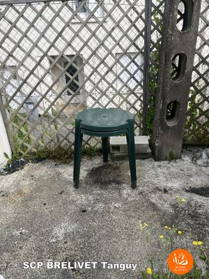un petit tabouret vert posé sur une terrasse en béton