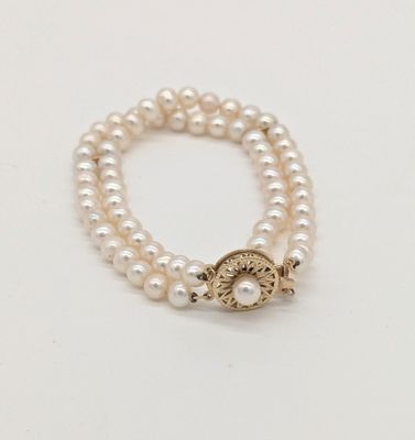 un gros plan sur un bracelet de perles blanches muni d'un fermoir en or