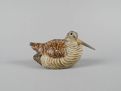 une petite figurine représentant un oiseau posé sur une surface blanche