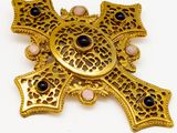 une photo d'une broche en forme de croix en or, ornée de pierres noires et roses