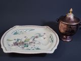 a plate with a flower design on it next to a silver urn