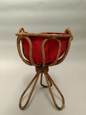 jardinière en corde avec un coussin rouge posée sur un support, sur fond blanc