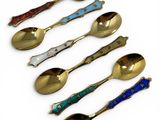 six spoons and a spoon rest in a row on a white surface