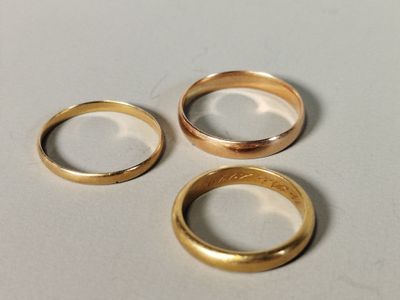 trois alliances en or posées sur une surface blanche