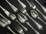 de nombreuses cuillères et fourchettes en argent posées sur une table noire
