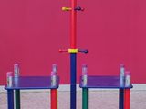 two colorful tables and a shelf in front of a pink wall